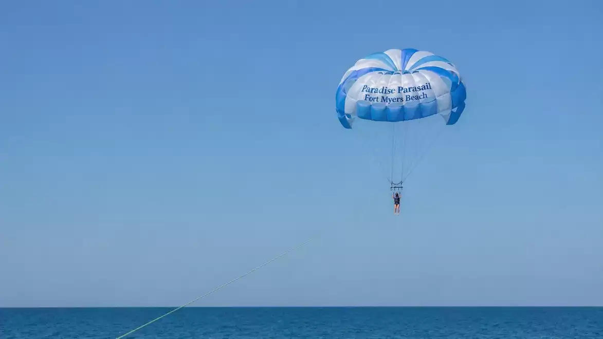 A person parasailing over the blue sea under a clear sky.