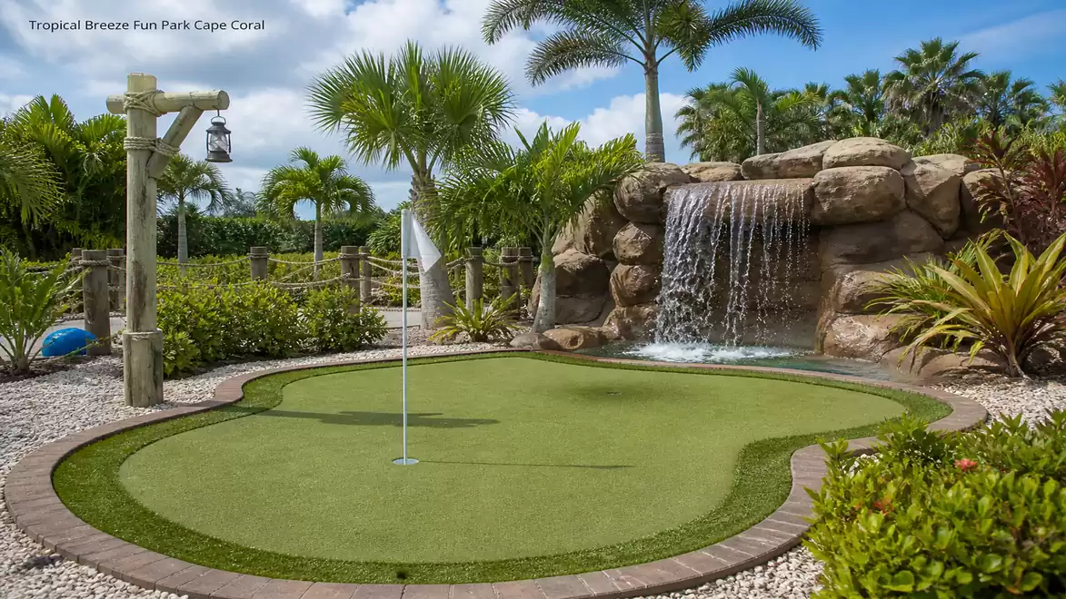 A mini golf course with palm trees and a small waterfall in the background, located in the Tropical Breeze Fun Park in Cape Coral.