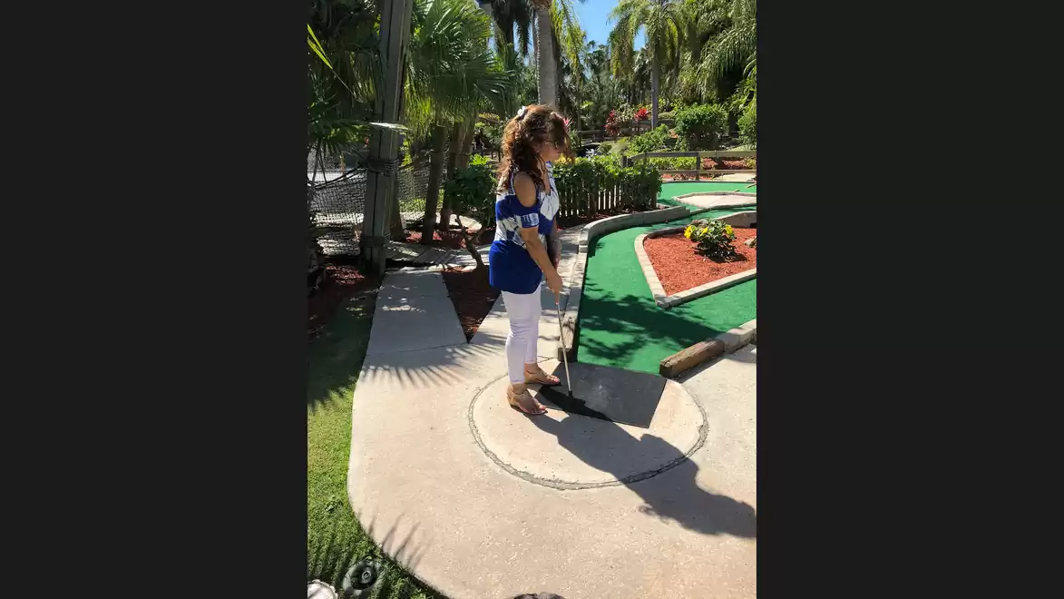 Woman playing mini-golf on a sunny, green course.