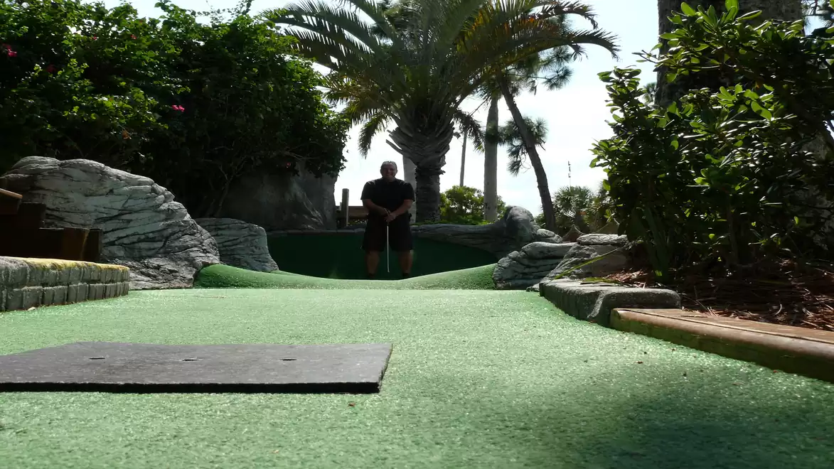 A miniature golf course photographed from the front. Palm trees and well-maintained bushes are visible in the background.