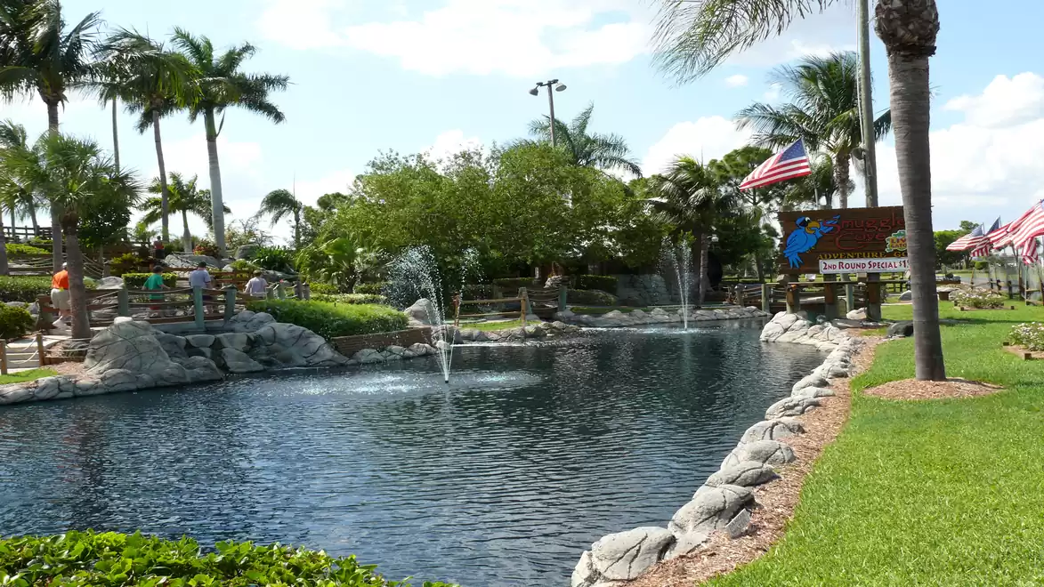 A picturesque pond with fountains surrounded by palm trees in a sunny park.