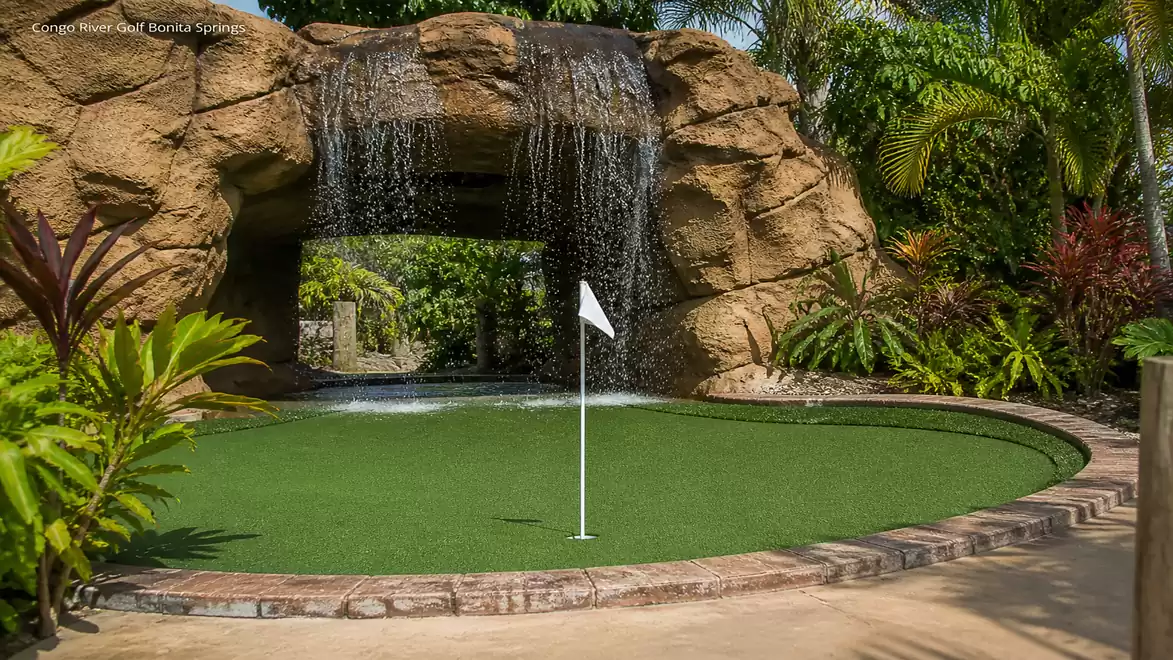 Mini golf course with green artificial turf, a waterfall, and tropical vegetation.