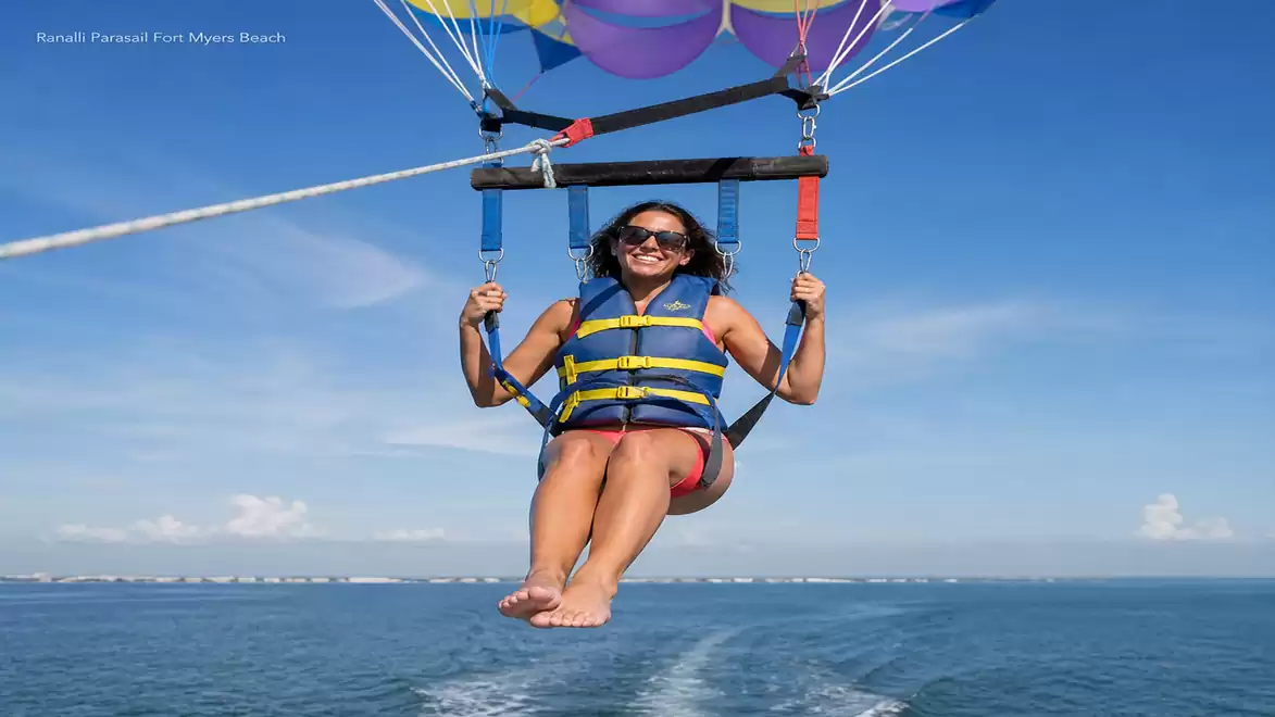 A woman enjoys parasailing with a colorful parachute over the open sea under a bright blue sky.