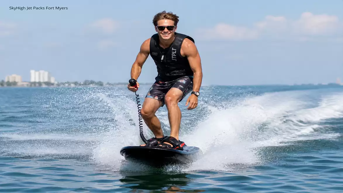 Man on a water jetboard gliding over calm sea under clear sky, wearing a black life vest and sunglasses.