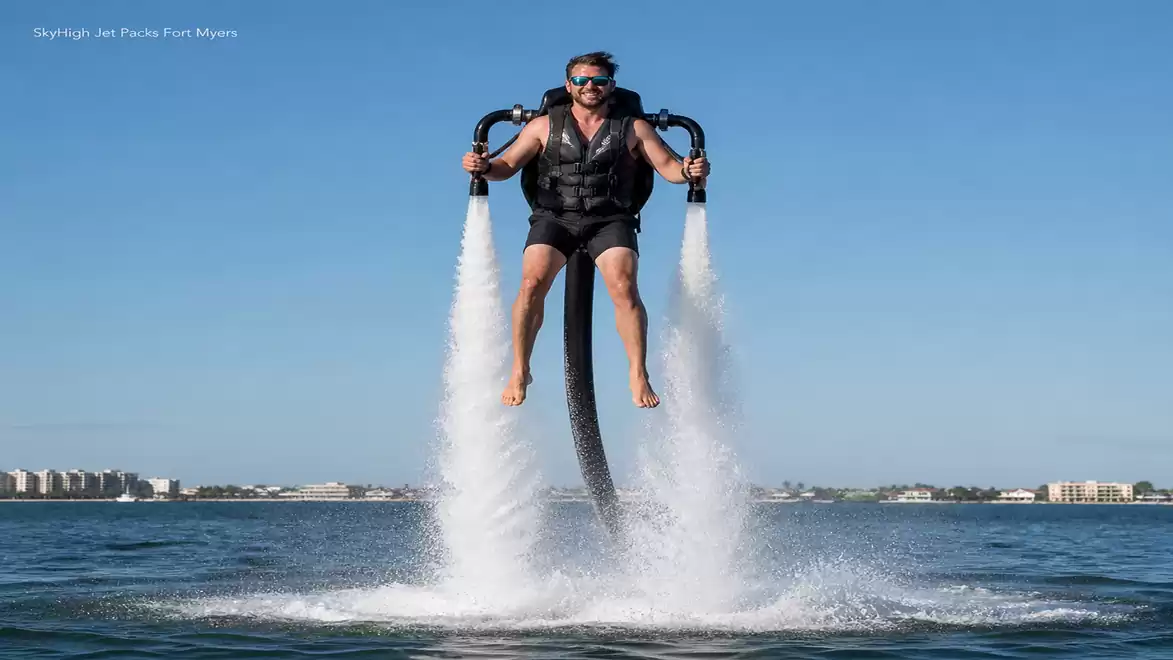 A man wearing sunglasses is flying with a water jetpack over the water on a sunny day.