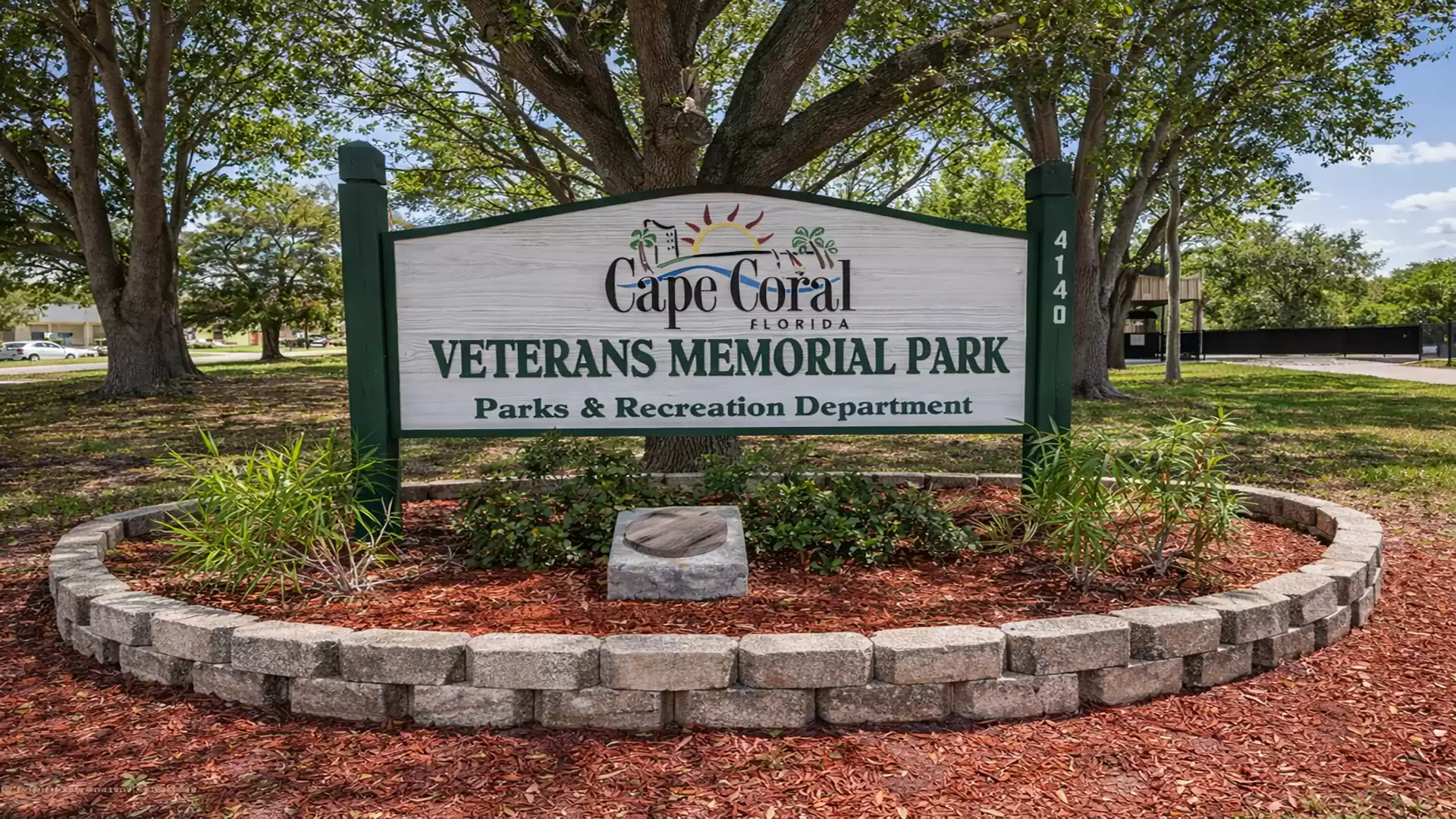 Entrance sign of Veterans Memorial Park in Cape Coral, surrounded by trees and plants.