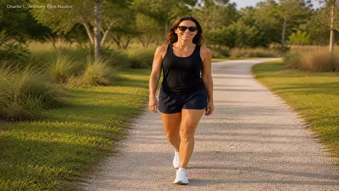 Woman walking on a nature path surrounded by trees and grass in sunny weather.