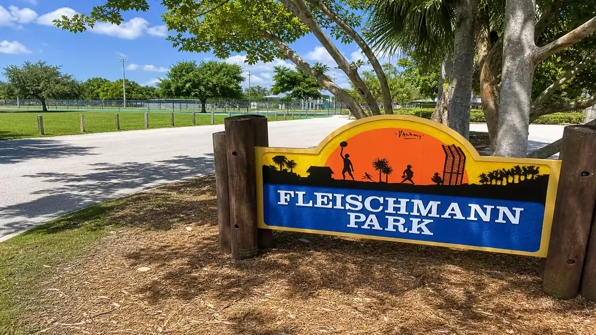 An entrance sign to Fleischmann Park with blue sky and trees in the background.