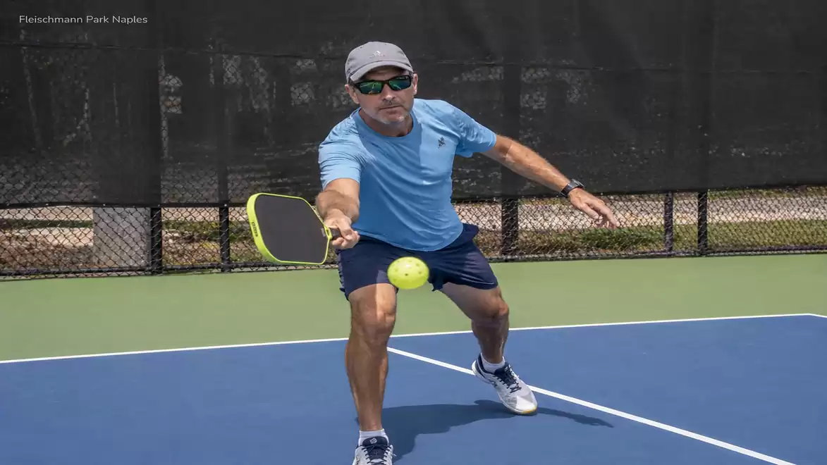 A man in blue sportswear plays pickleball on a tennis court.