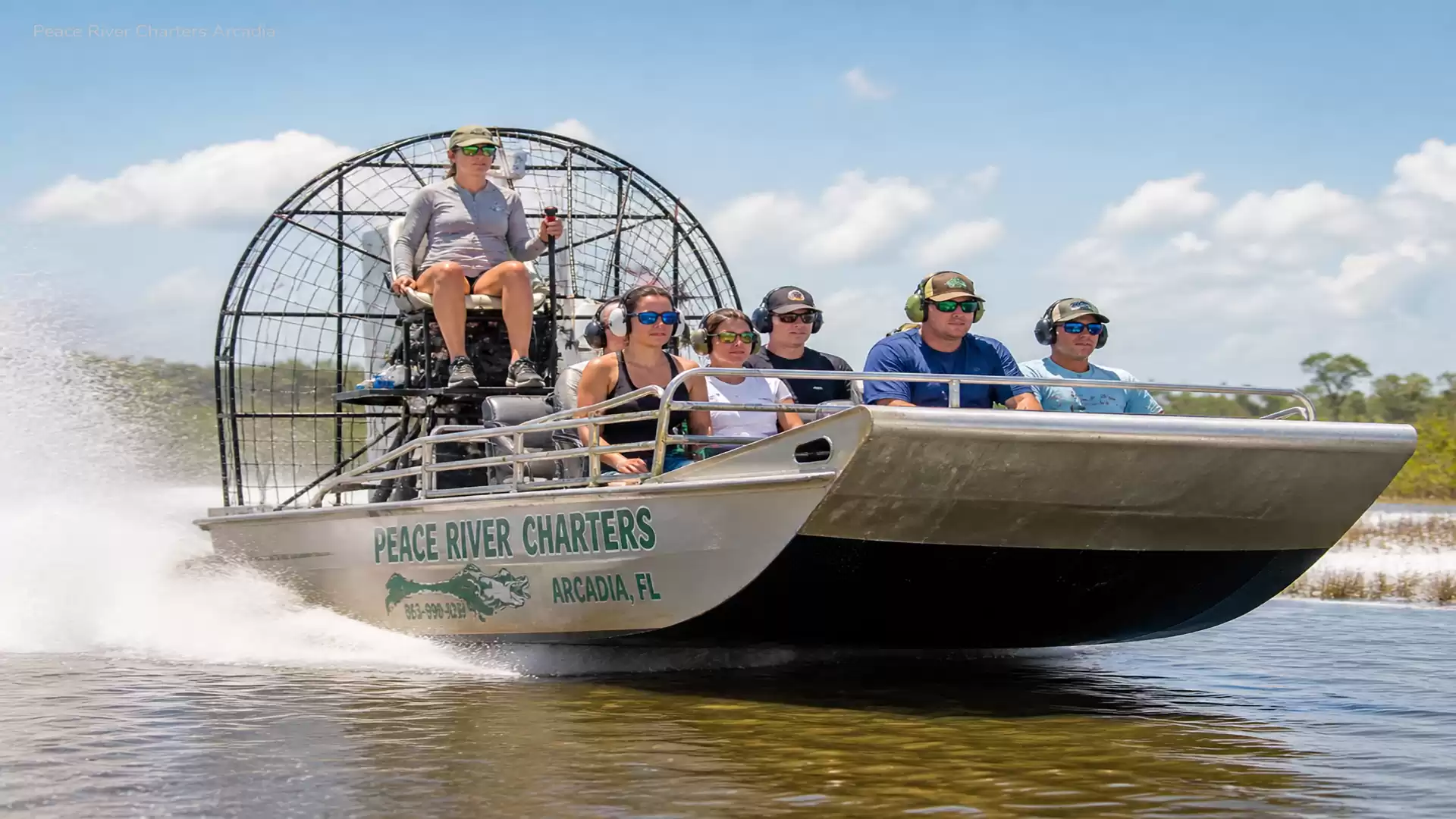 A group of people riding an airboat on a river in sunny weather.