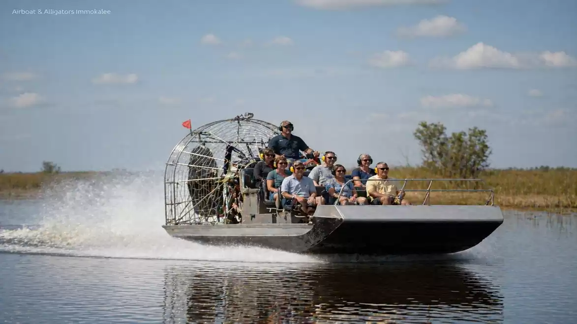 A group of people on an airboat traveling through a body of water in an open landscape with clear skies.
