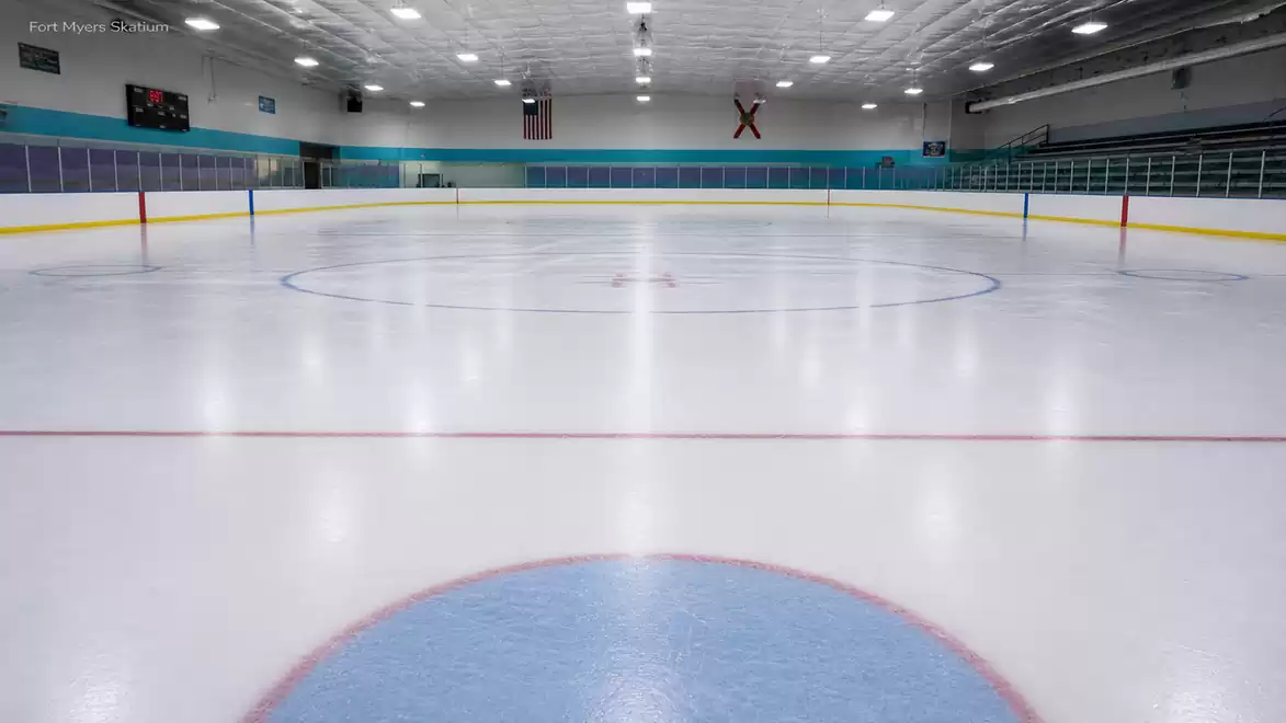 Empty ice hockey arena with smooth ice surface, marked zones, and illuminated ceiling.