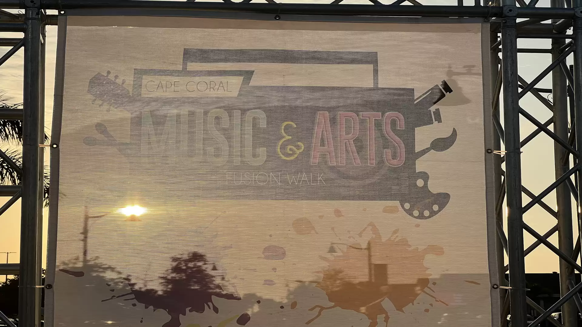 A festival stage with a music and arts poster at sunset.