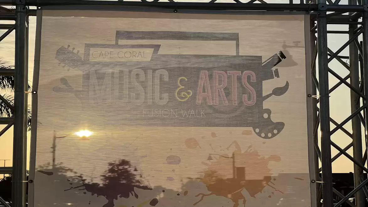 A festival stage with a music and arts poster at sunset.