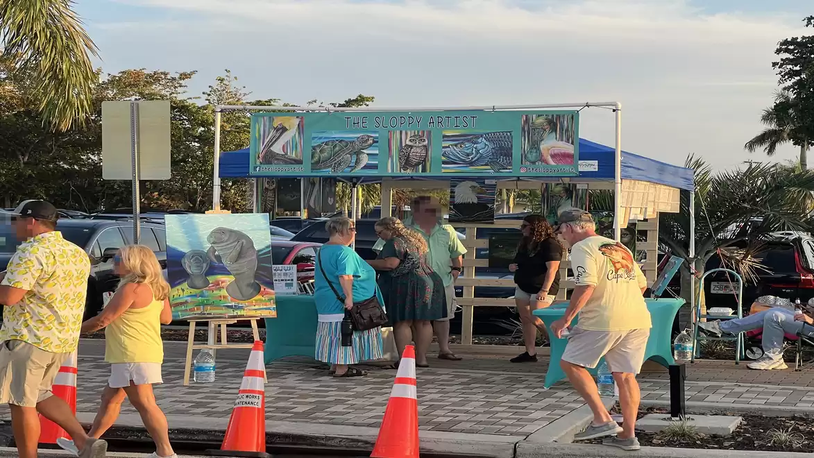 People visiting a street stall with artworks at a sunny street festival.