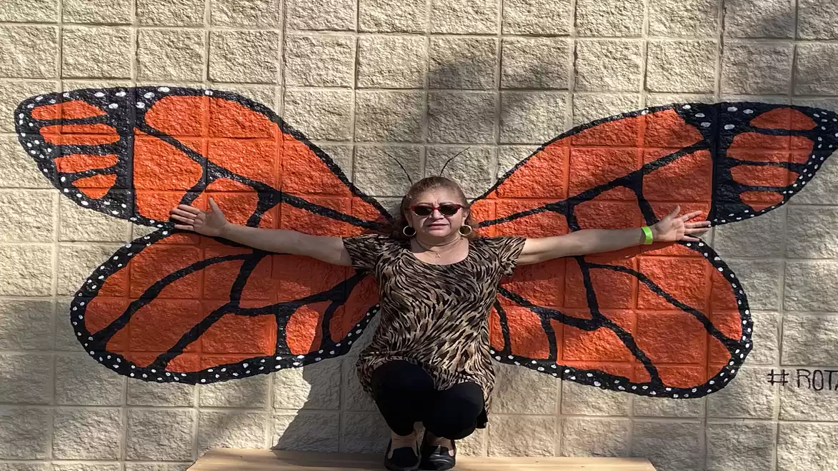 Person posing in front of a wall with butterfly wings, arms outstretched.