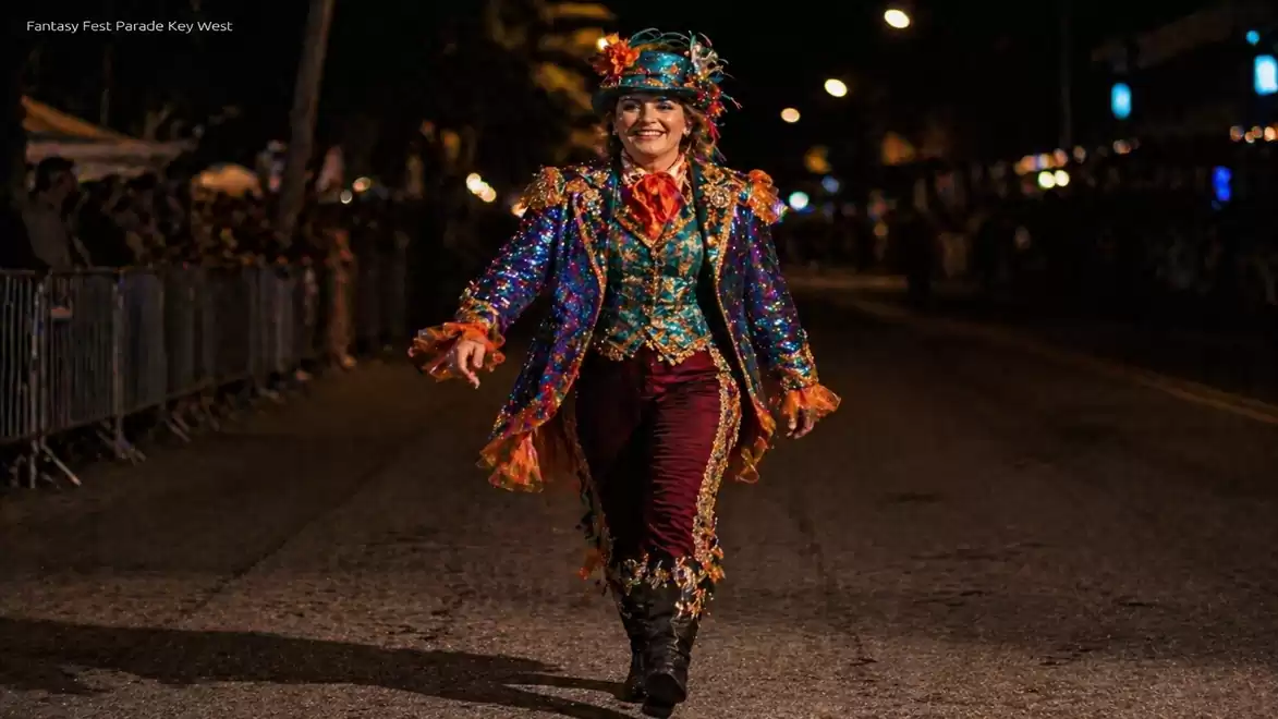 A person in a colorful, festive costume walks on a street at night during a parade.