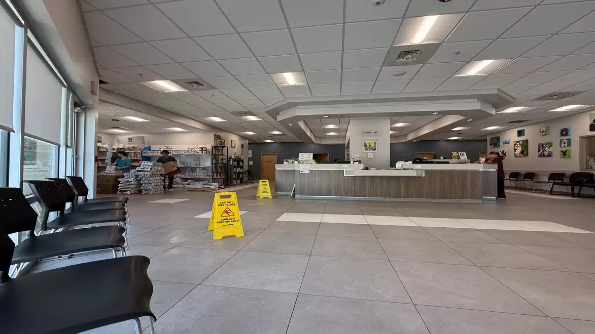 Interior view of a modern, spacious reception area with seating, warning signs on the floor, and a reception desk in the background.