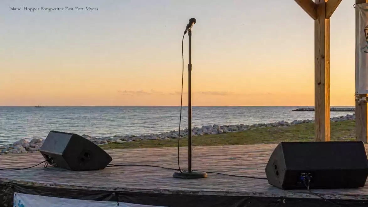 An empty stage at sunset with a microphone stand and speakers by the sea.