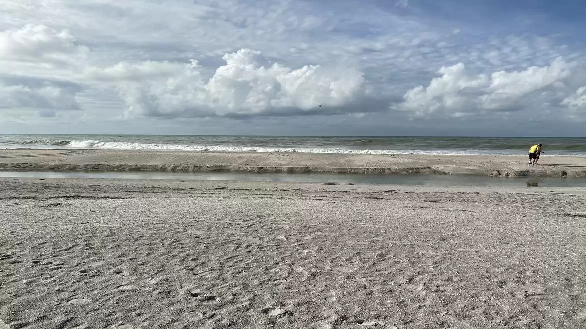 A vast, calm beach with a cloudy sky and a person in the distance.