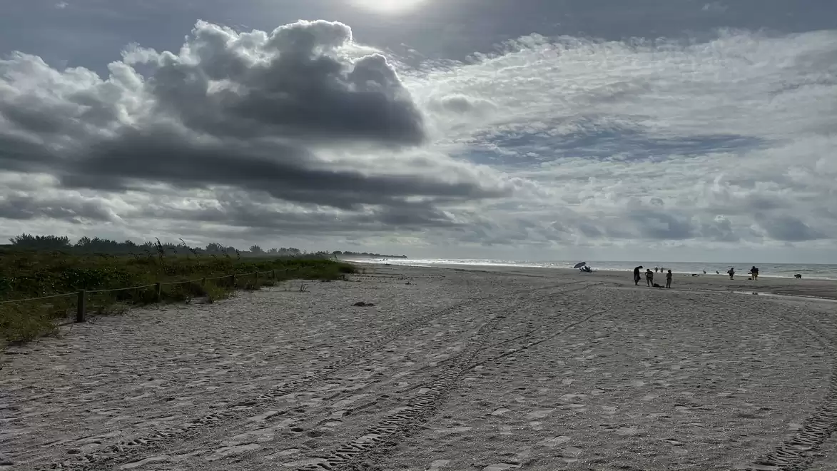 A sandy beach with clouds in the sky and several people in the distance.