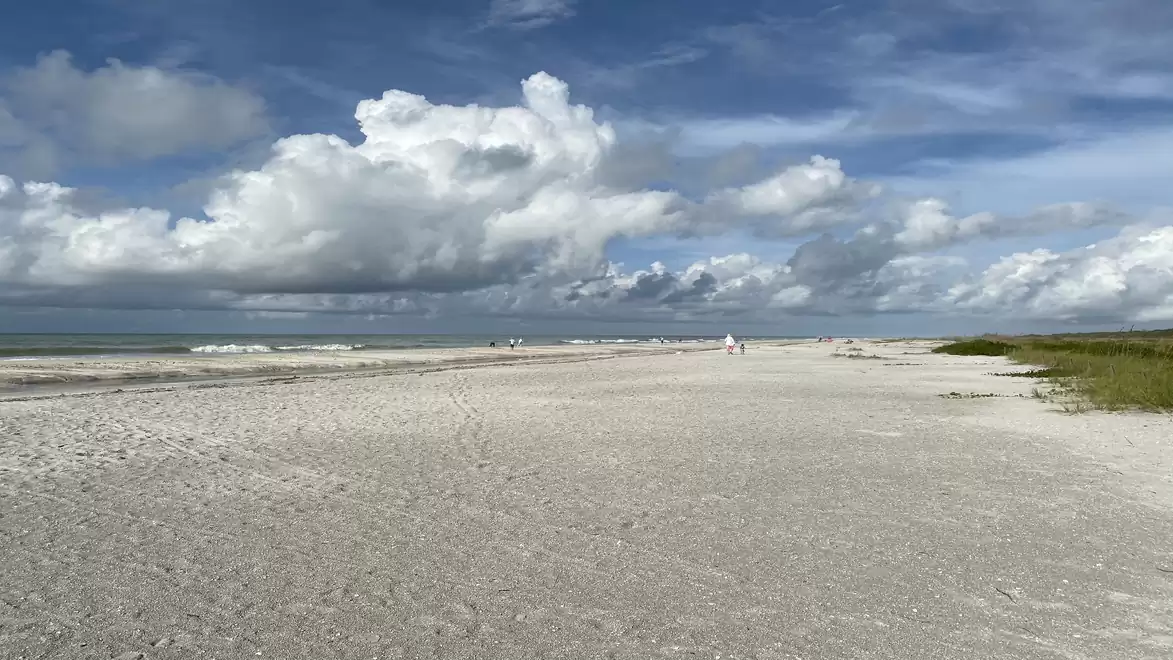 White sandy beach with blue sky and white clouds on the horizon.
