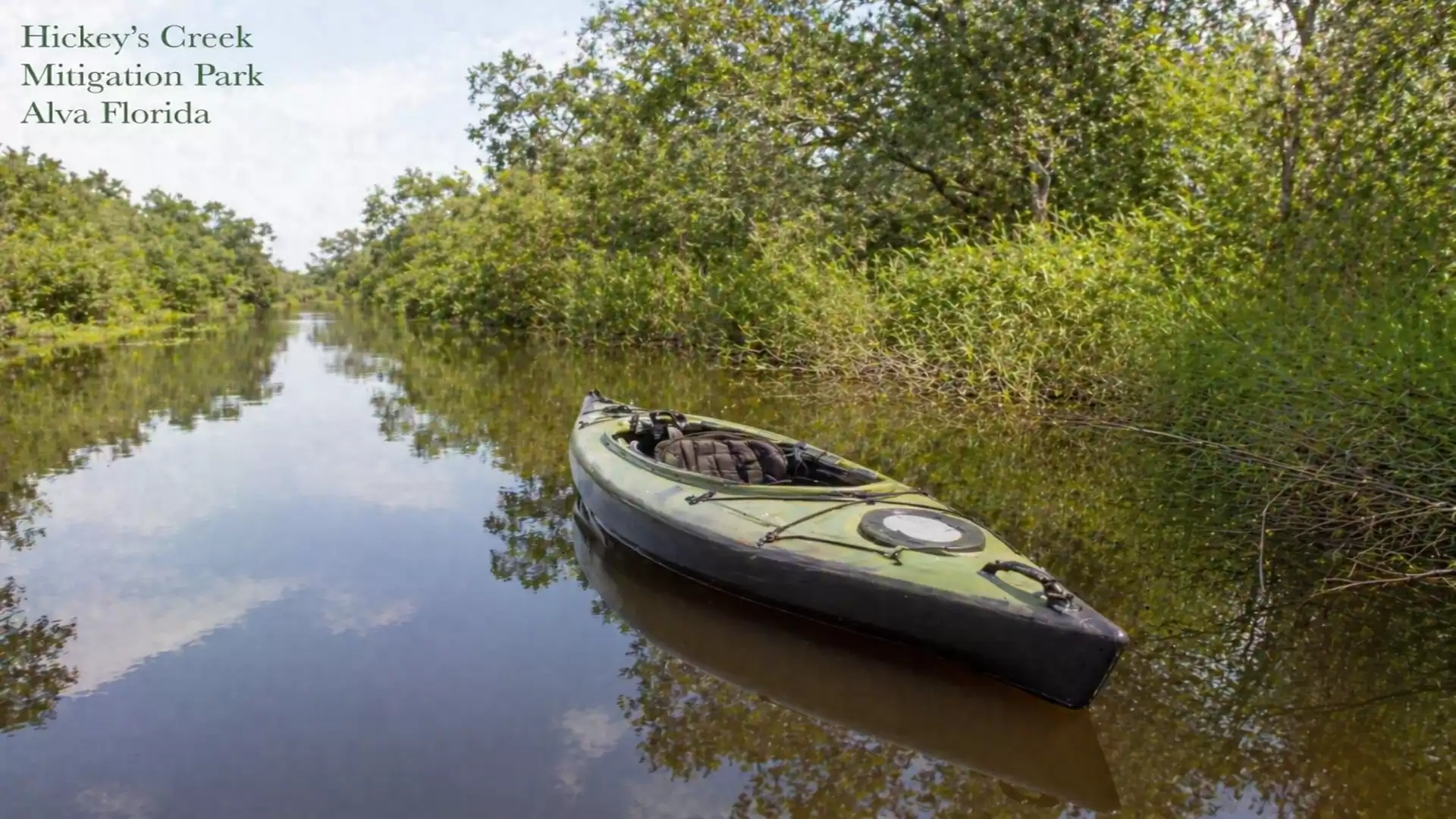 A green kayak floats serenely on a wide river in a lush river landscape at Hickey's Creek Mitigation Park, Alva, Florida.