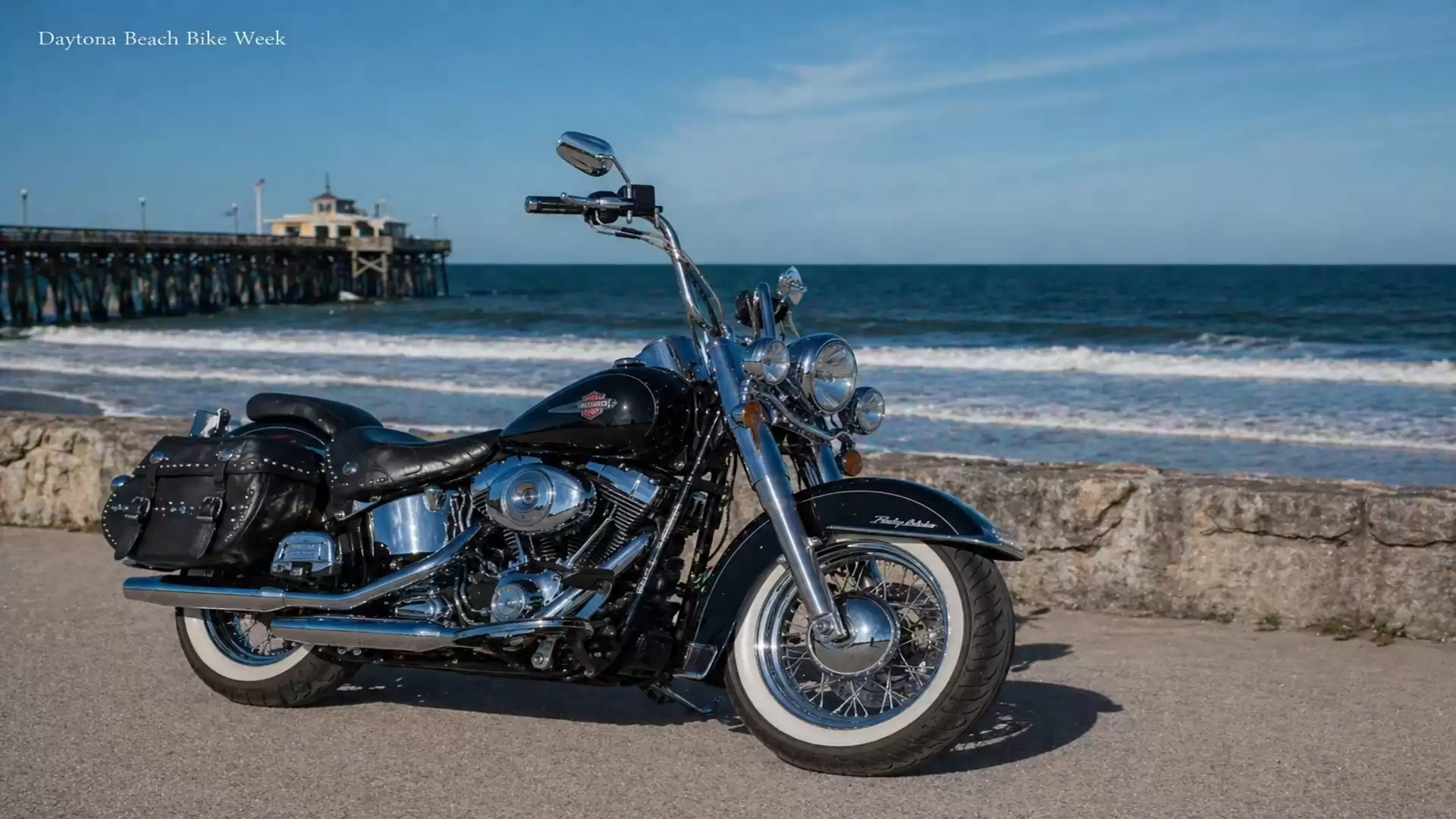 A shiny motorcycle stands in front of a scenic beach setting with blue sky and calm sea during the Daytona Beach Bike Week.