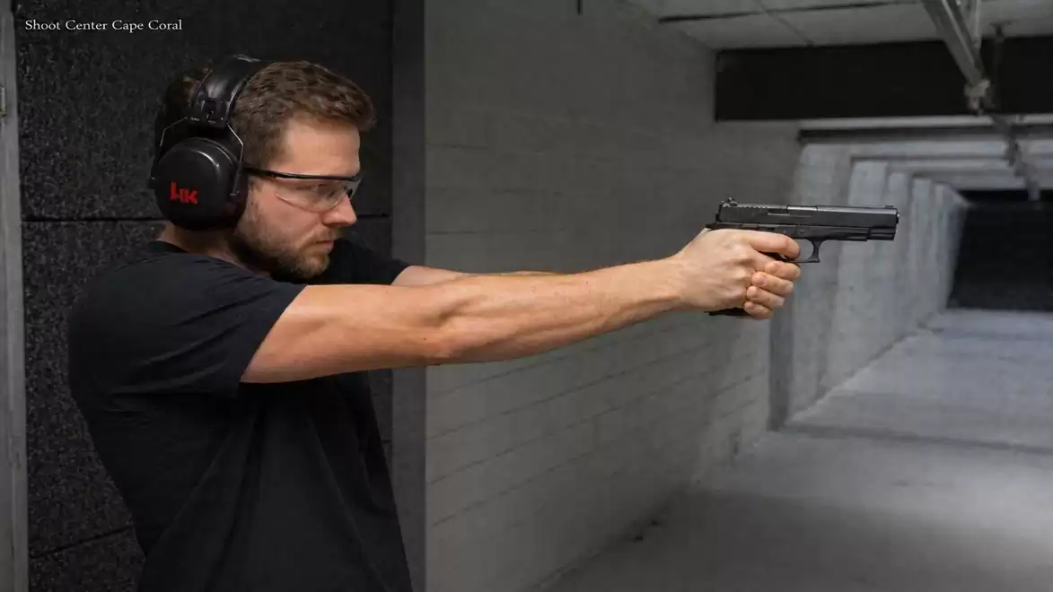 Man practicing shooting at a shooting range with a pistol, wearing ear protection and safety glasses.