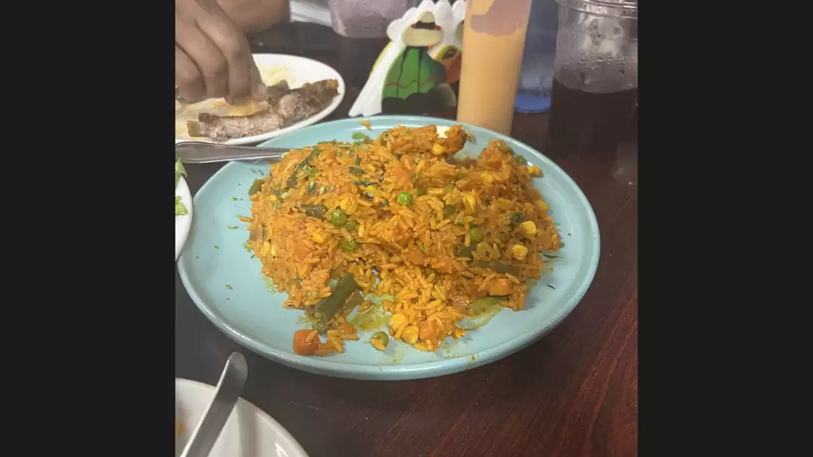 A plate of spicy yellow rice and herbs on a table, next to a hand with bread.
