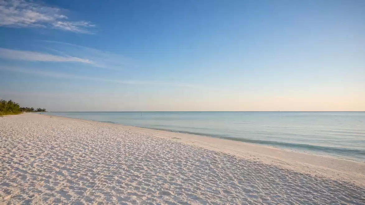 A tranquil sandy beach under a blue sky with gentle waves in the sea.