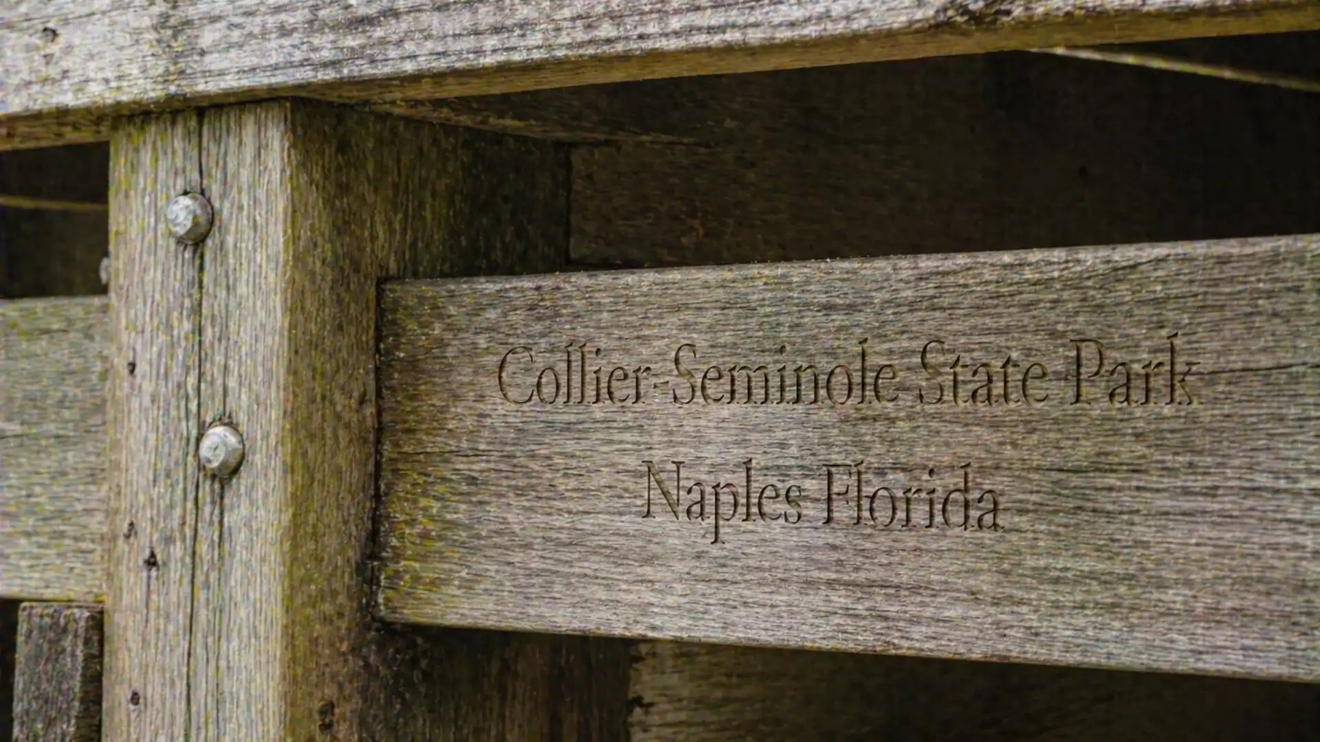 A weathered wooden sign with the inscription 'Collier-Seminole State Park Naples Florida', part of a wooden structure.