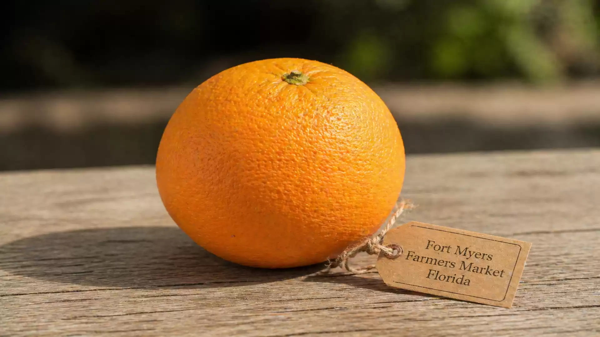 A fresh orange with a tag from the Fort Myers Farmers Market in Florida on a wooden table.