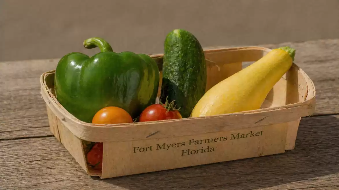 Fresh vegetables in a wooden basket from Fort Myers Farmers Market, including bell pepper, cucumber, tomato, and yellow zucchini.