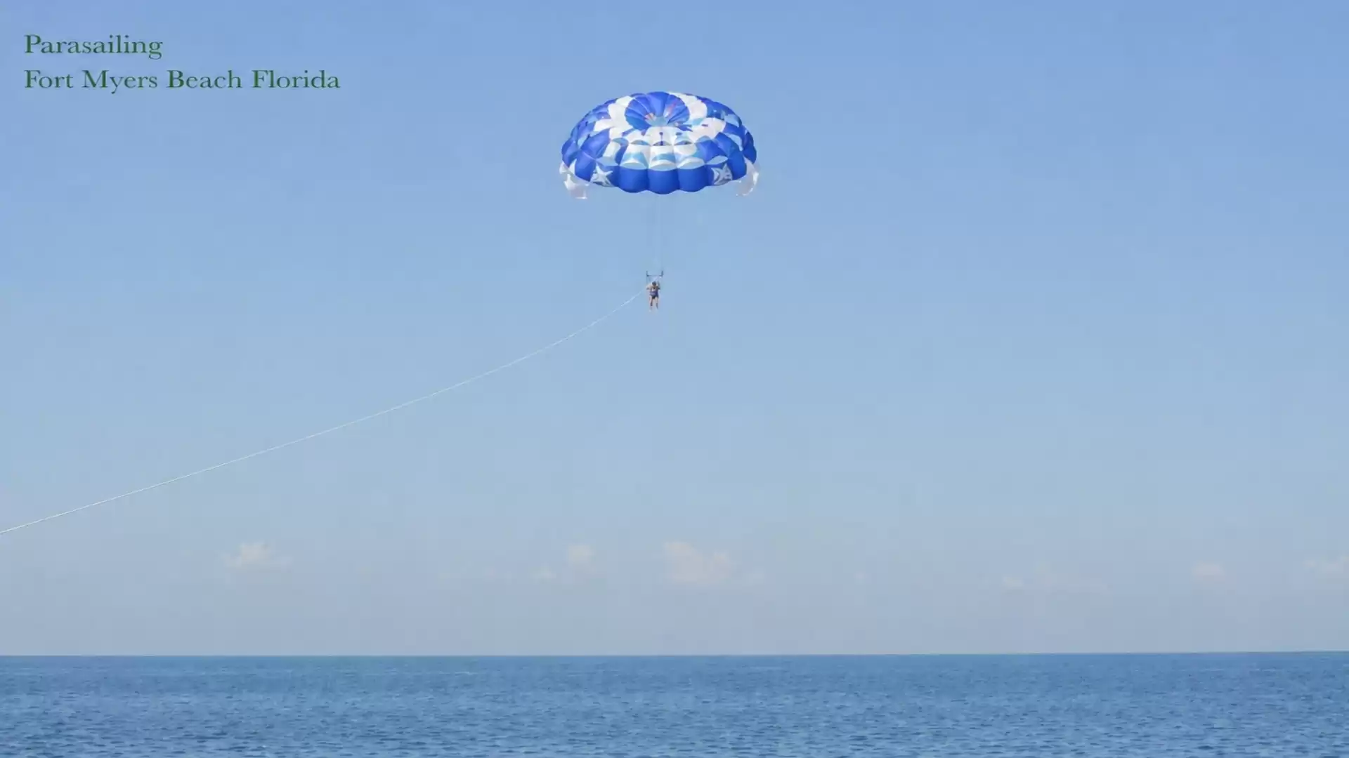 A blue parachute for parasailing over the clear waters of Fort Myers Beach, Florida, under a clear sky.