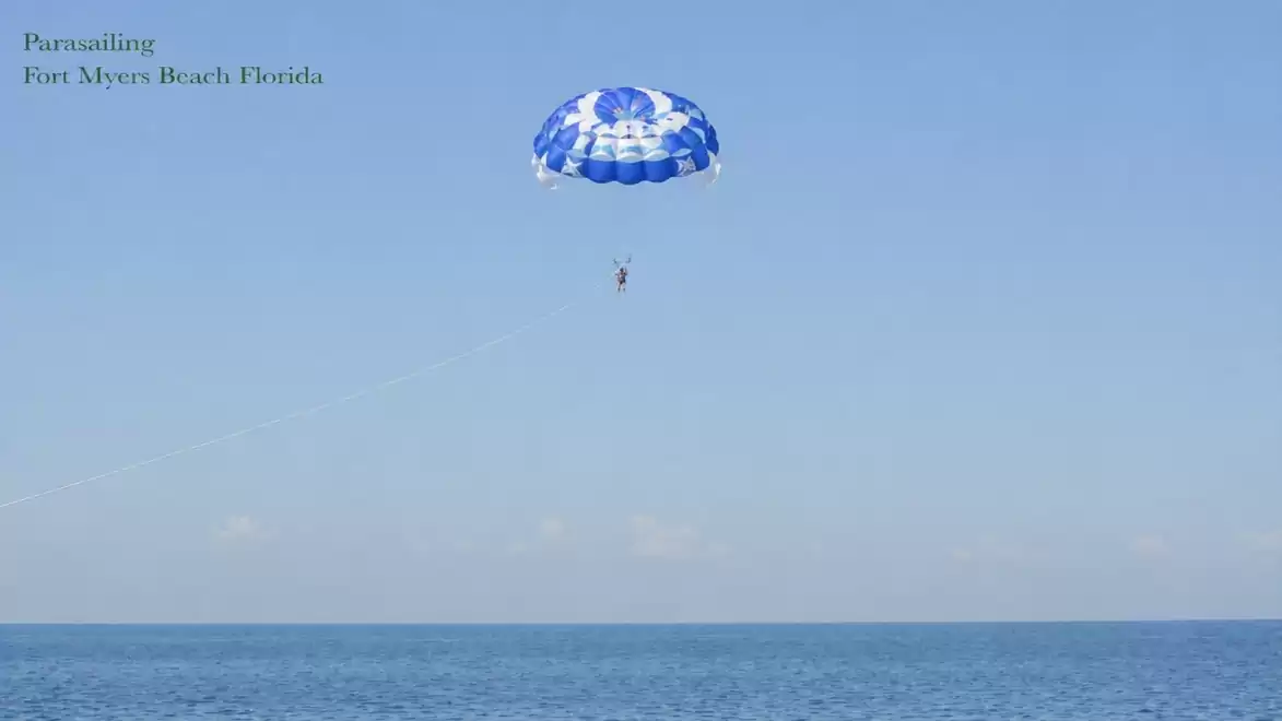 A blue parachute for parasailing over the clear waters of Fort Myers Beach, Florida, under a clear sky.