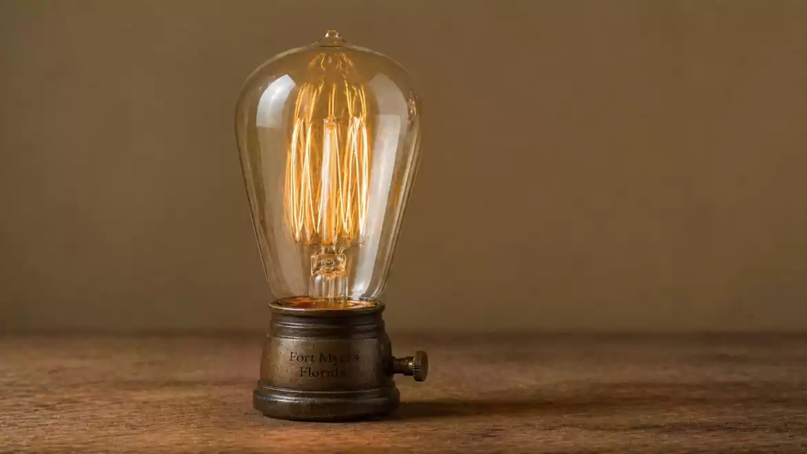 A vintage light bulb on a wooden surface emitting warm light with a minimalist design.