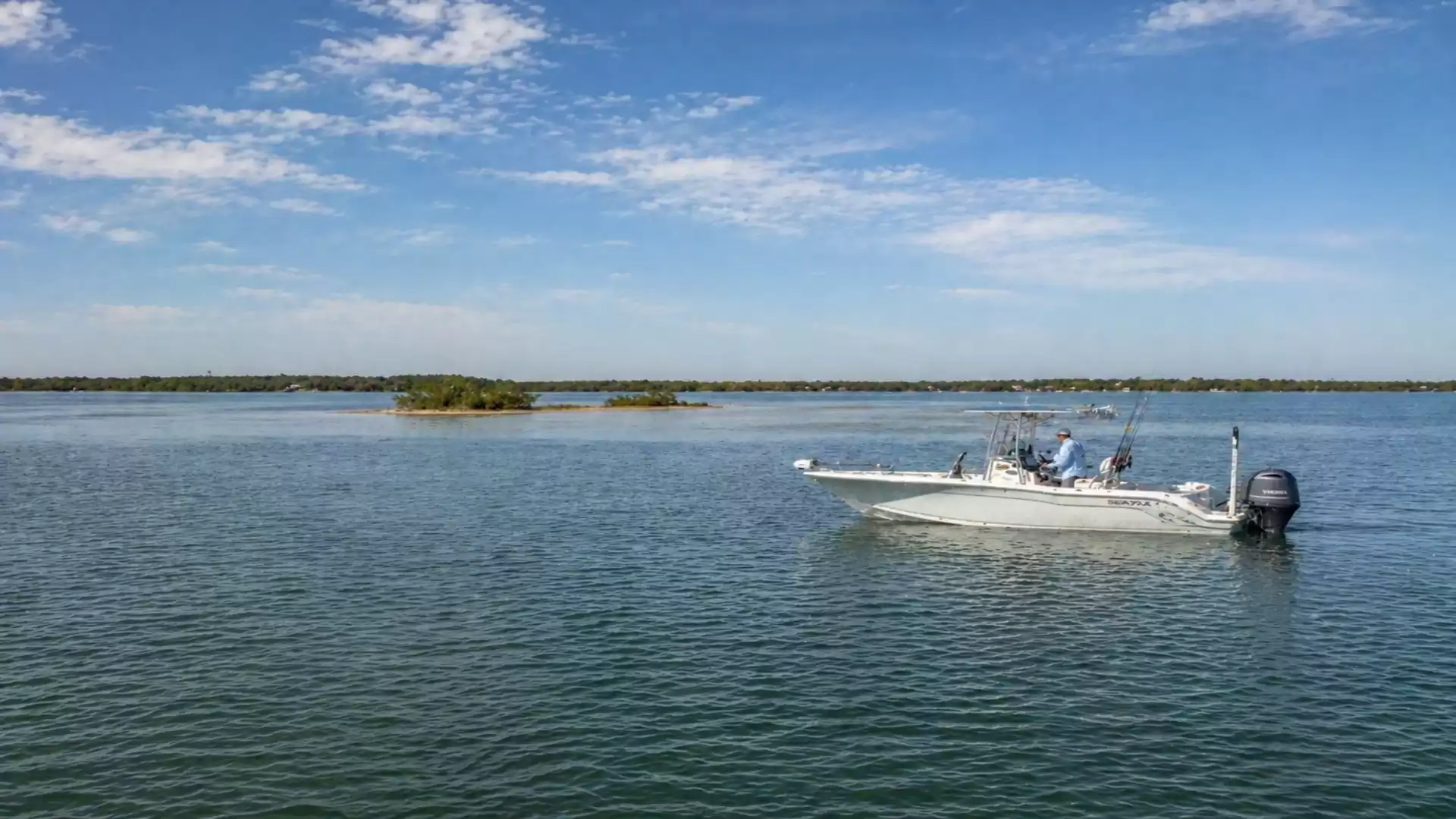 A boat sails on a wide lake under a clear blue sky with scattered clouds and small islands in the background.