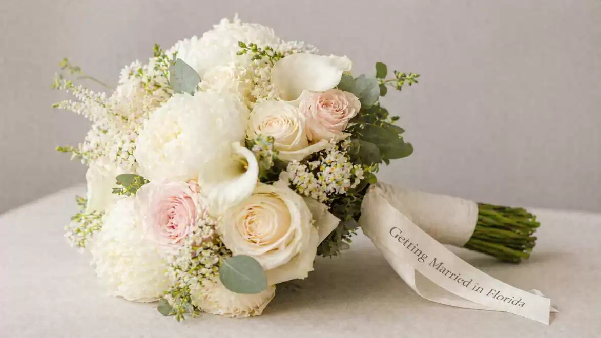 An elegant bridal bouquet with white and pink flowers, including roses and calla lilies, tied with a ribbon reading 'Getting Married in Florida'.