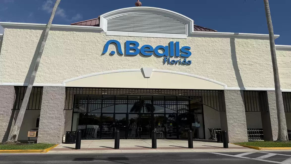 Front view of a store named 'Bealls Homes' under a clear blue sky, with palm trees on the sides.