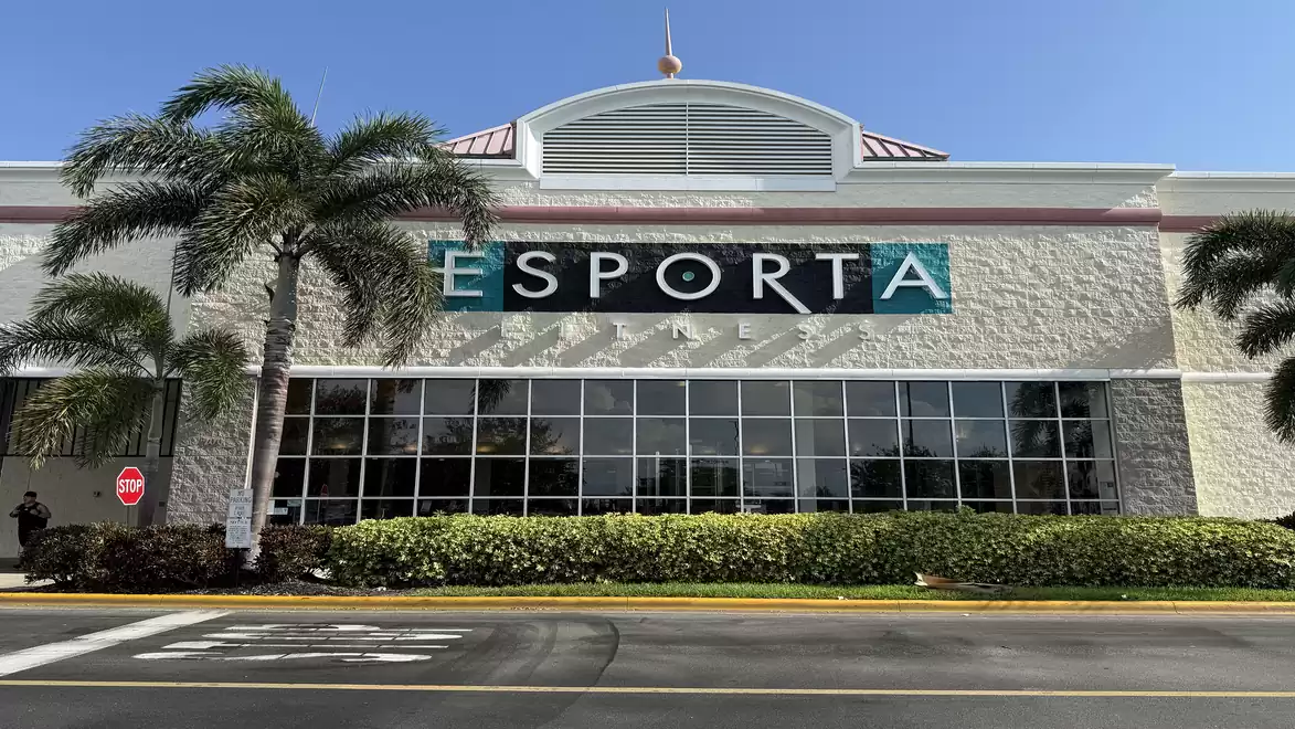 Exterior view of a gym called Esporta with palm trees in the foreground.