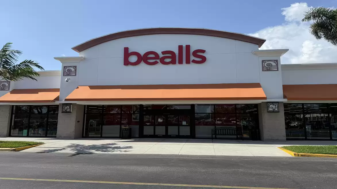 Exterior view of a retail store with a large red 'bealls' sign above the entrance, blue sky in the background.