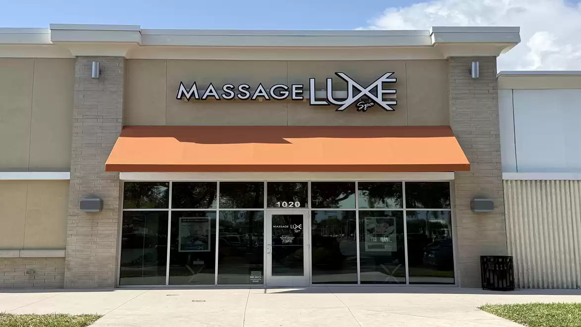 Exterior view of a massage spa shop with an orange awning and large glass facade.