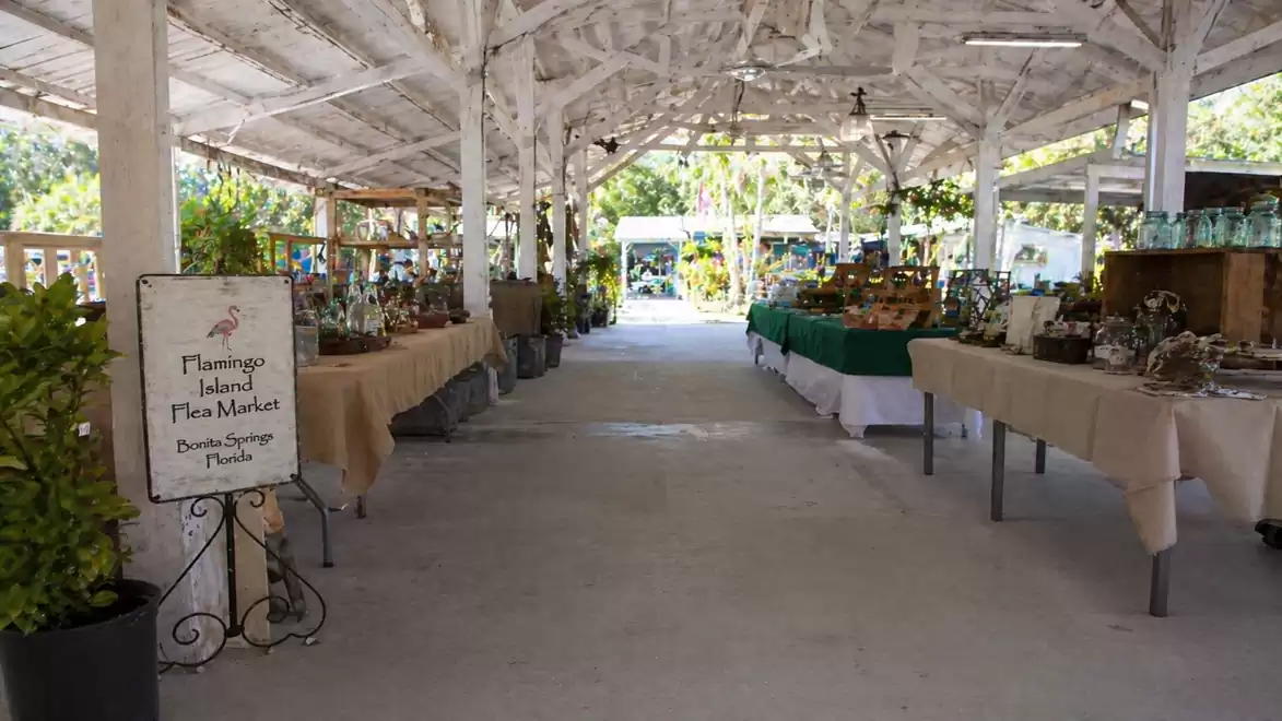 Covered flea market with tables full of goods and a sign reading 'Flamingo Island Flea Market'.