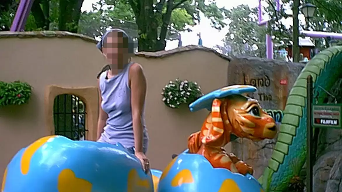 A person sitting on a colorful ride in an amusement park, surrounded by trees and decorative elements.