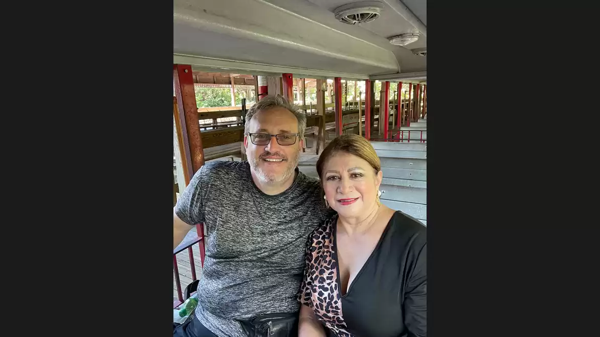 A couple smiling while sitting in an open train car with red metal railings.