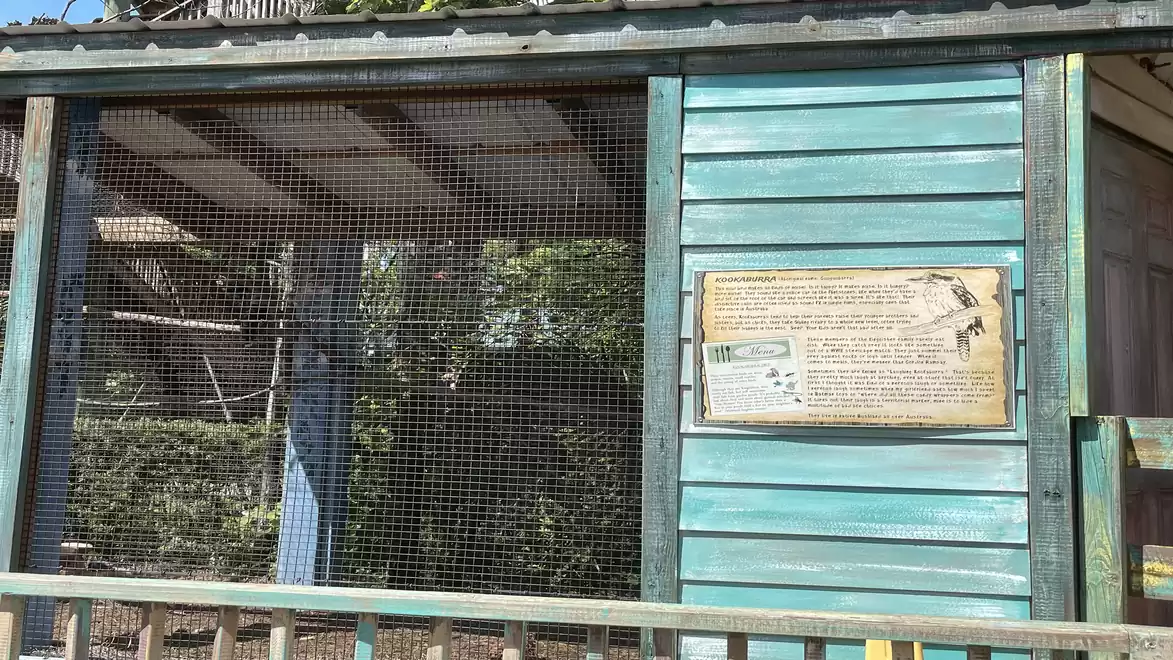 Wooden building with blue paint, partially covered with wire mesh, next to an informational sign.