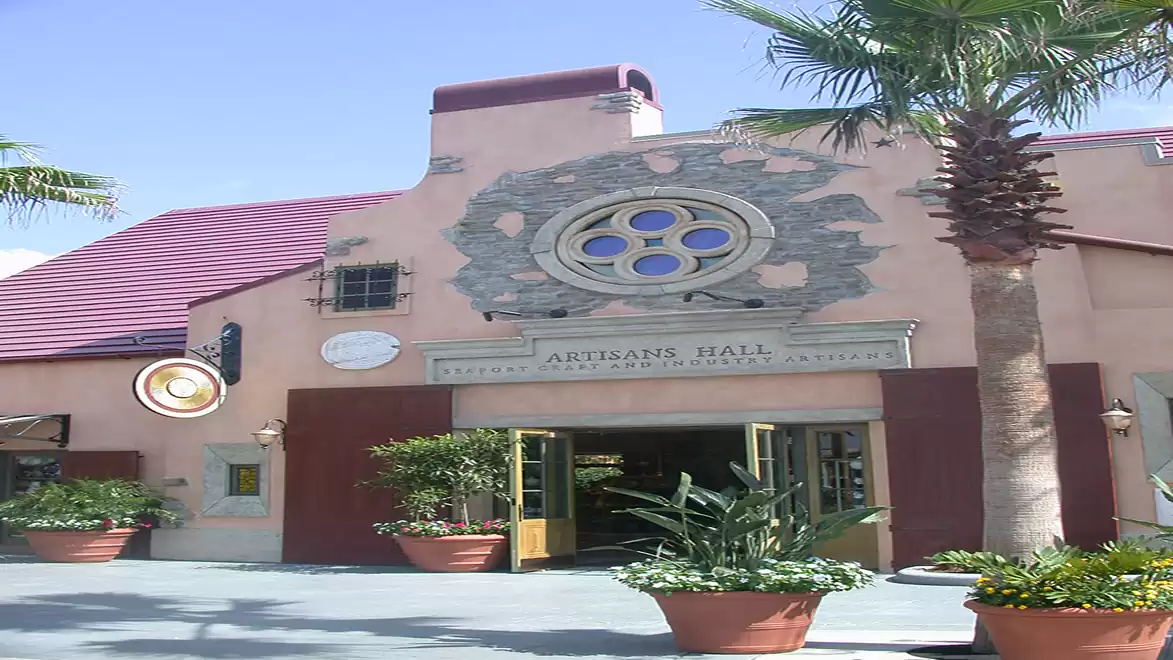 A building with a decorative window and an entrance with plants. The building has a red roof and is surrounded by palm trees.