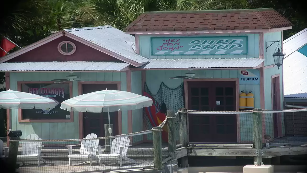 Colorful surf shop hut with two umbrellas and lounge chairs in the foreground.