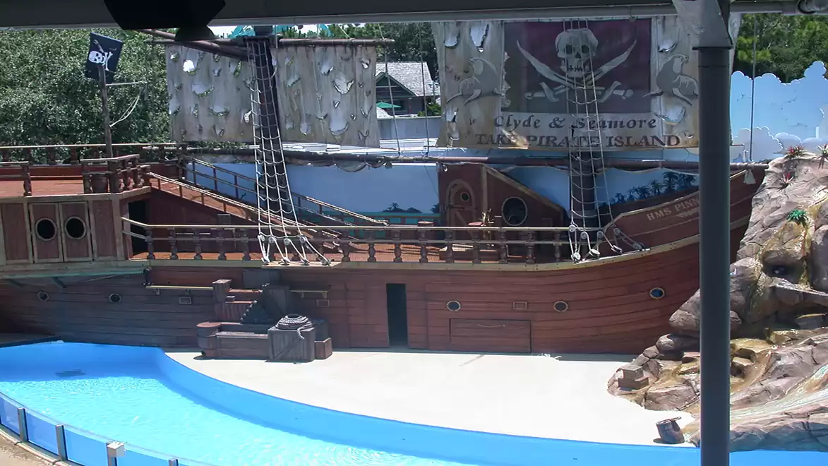 A large pirate ship replica with rigging and a skull banner. The ship is situated in a water park setting.
